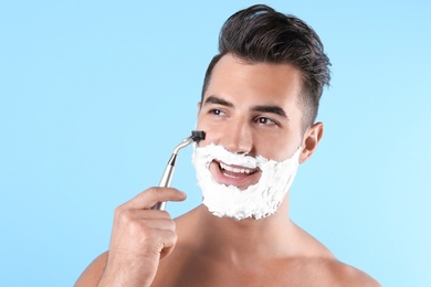 Handsome young man shaving on color background