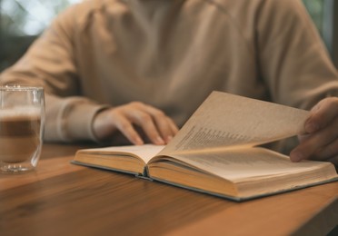 Image of Man with coffee reading book at wooden table, closeup