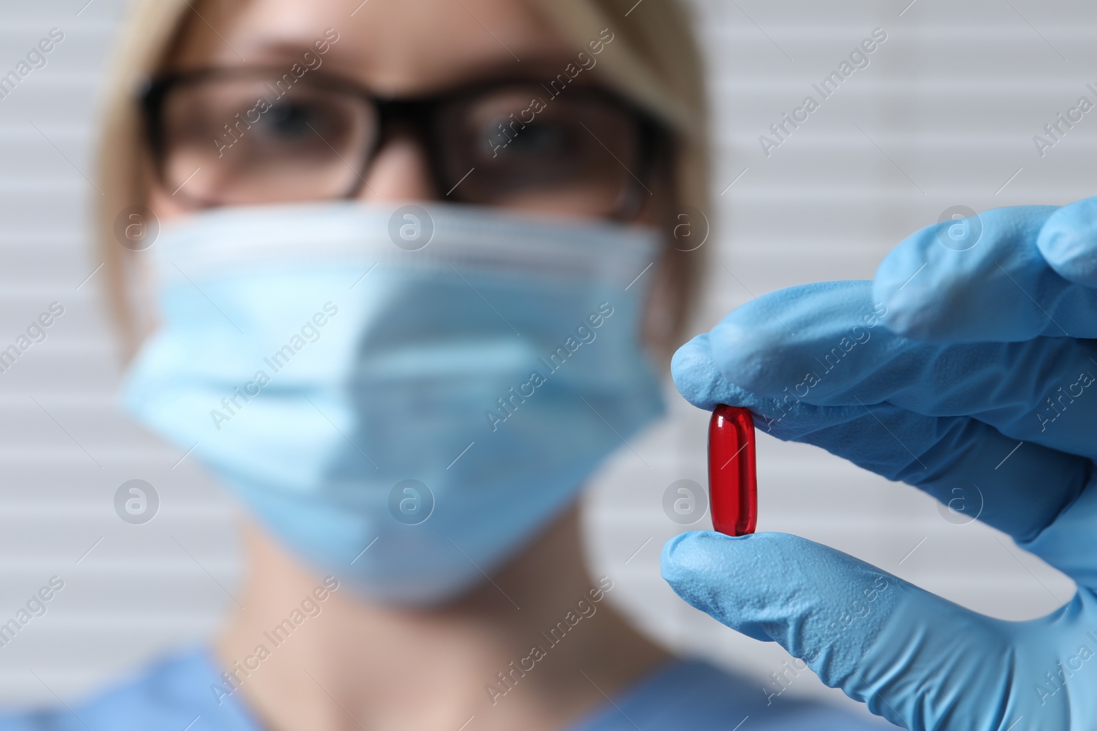 Photo of Doctor holding pill on light background, selective focus. Space for text