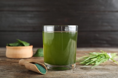 Photo of Glass of spirulina drink, scoop with powder and wheat grass on wooden table