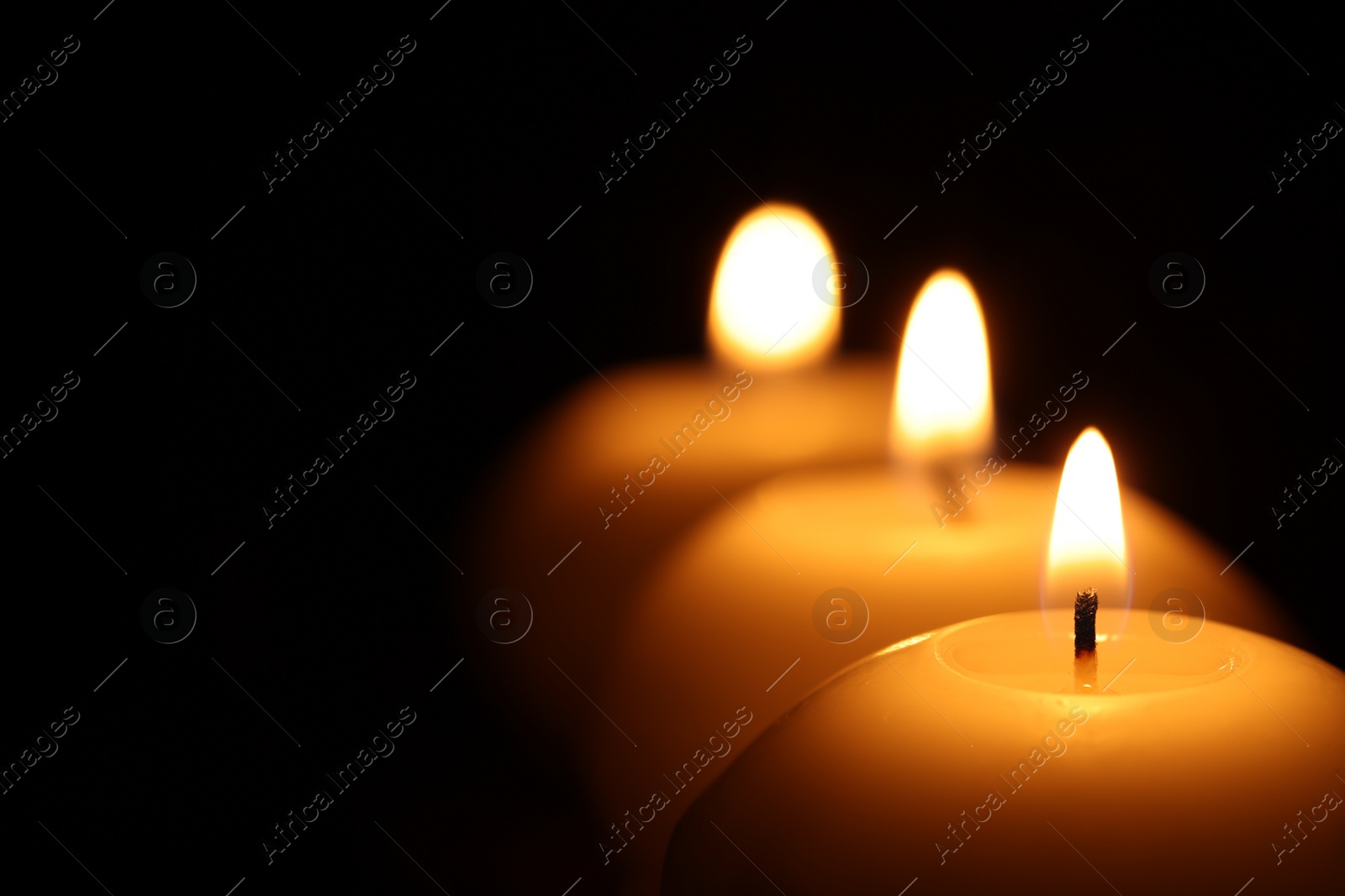 Photo of Burning wax candles on black background, closeup. Space for text