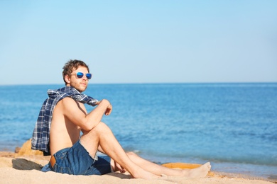 Photo of Young man sitting on beach. Space for text
