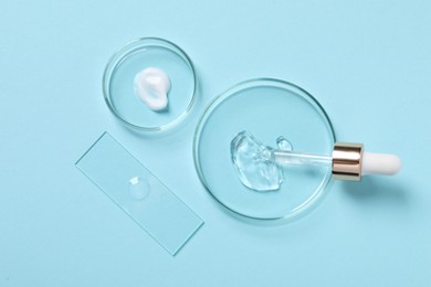 Photo of Petri dishes with samples of cosmetic serums and pipette on light blue background, flat lay