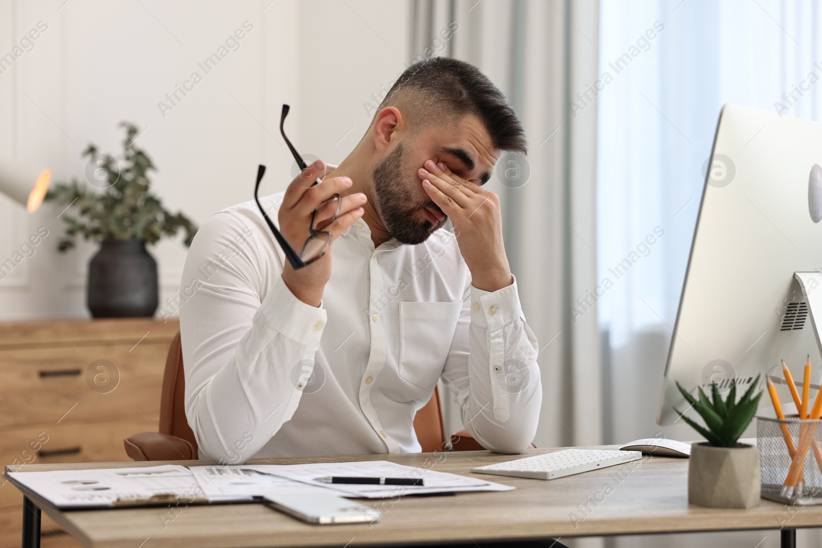 Photo of Overwhelmed man with glasses sitting at table in office