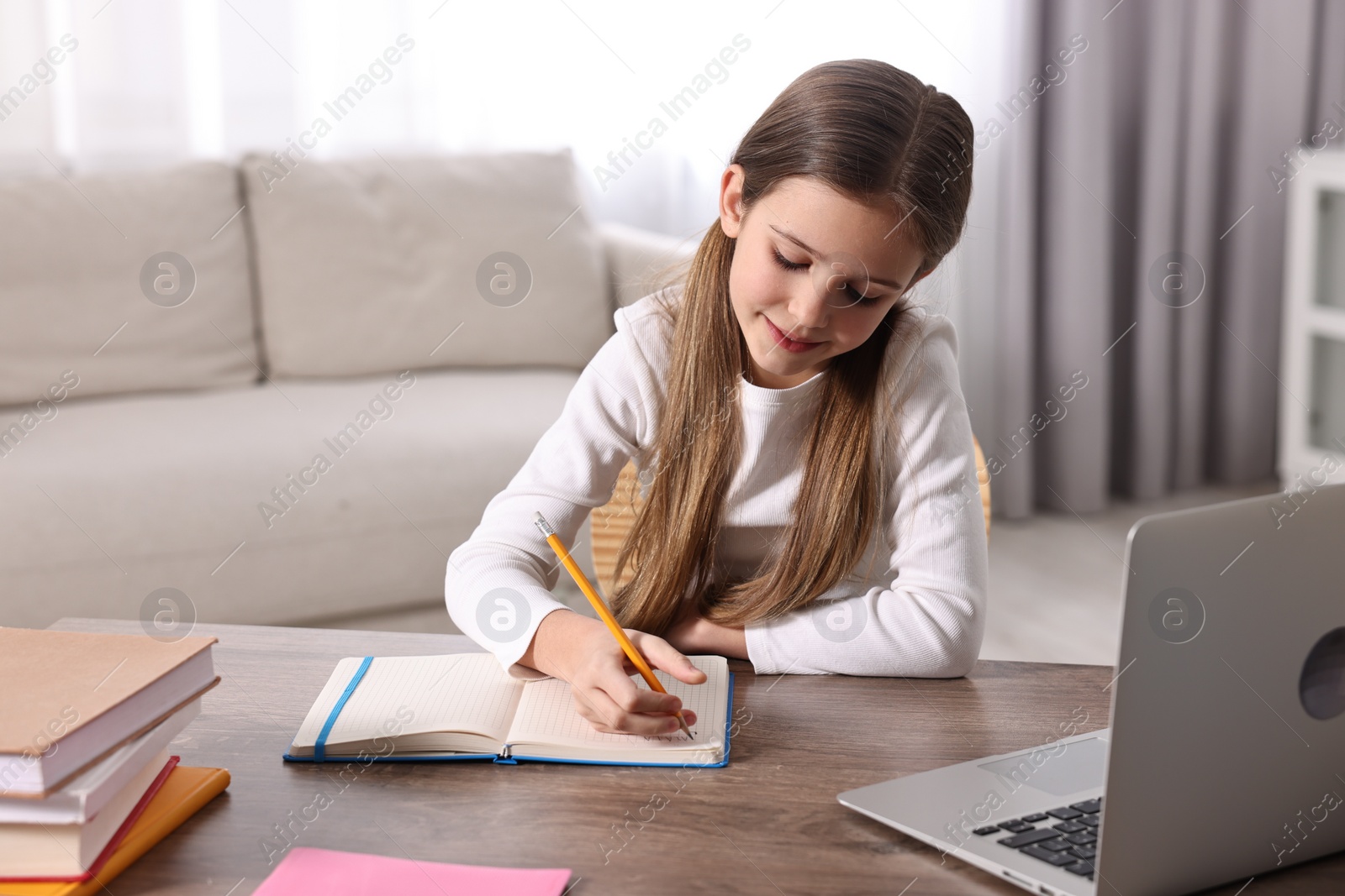 Photo of E-learning. Cute girl taking notes during online lesson at table indoors