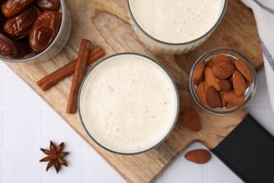 Photo of Glasses of delicious date smoothie, dried fruits, spices and nuts on white tiled table, flat lay