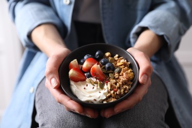 Woman holding bowl of tasty granola with berries, yogurt and seeds, closeup