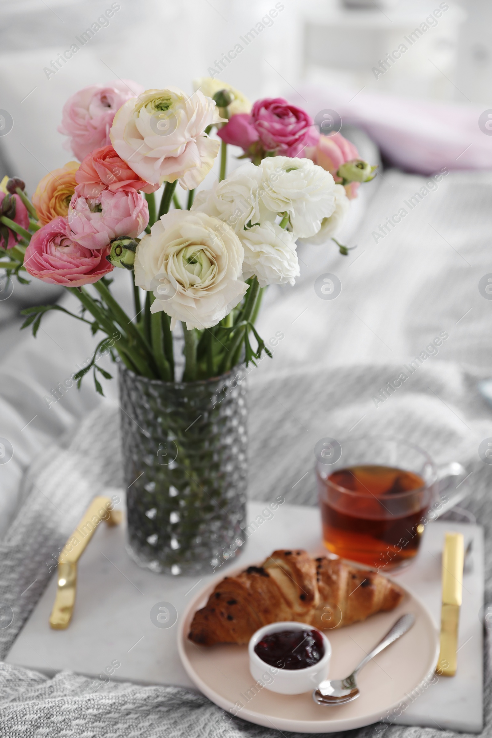 Photo of Bouquet of beautiful ranunculuses, croissant and tea on bed indoors