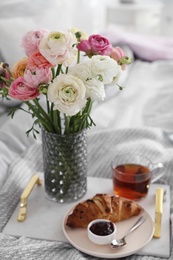 Bouquet of beautiful ranunculuses, croissant and tea on bed indoors