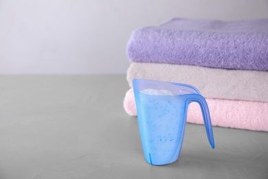 Photo of Measuring cup of laundry powder and clean towels on grey table against light background. Space for text