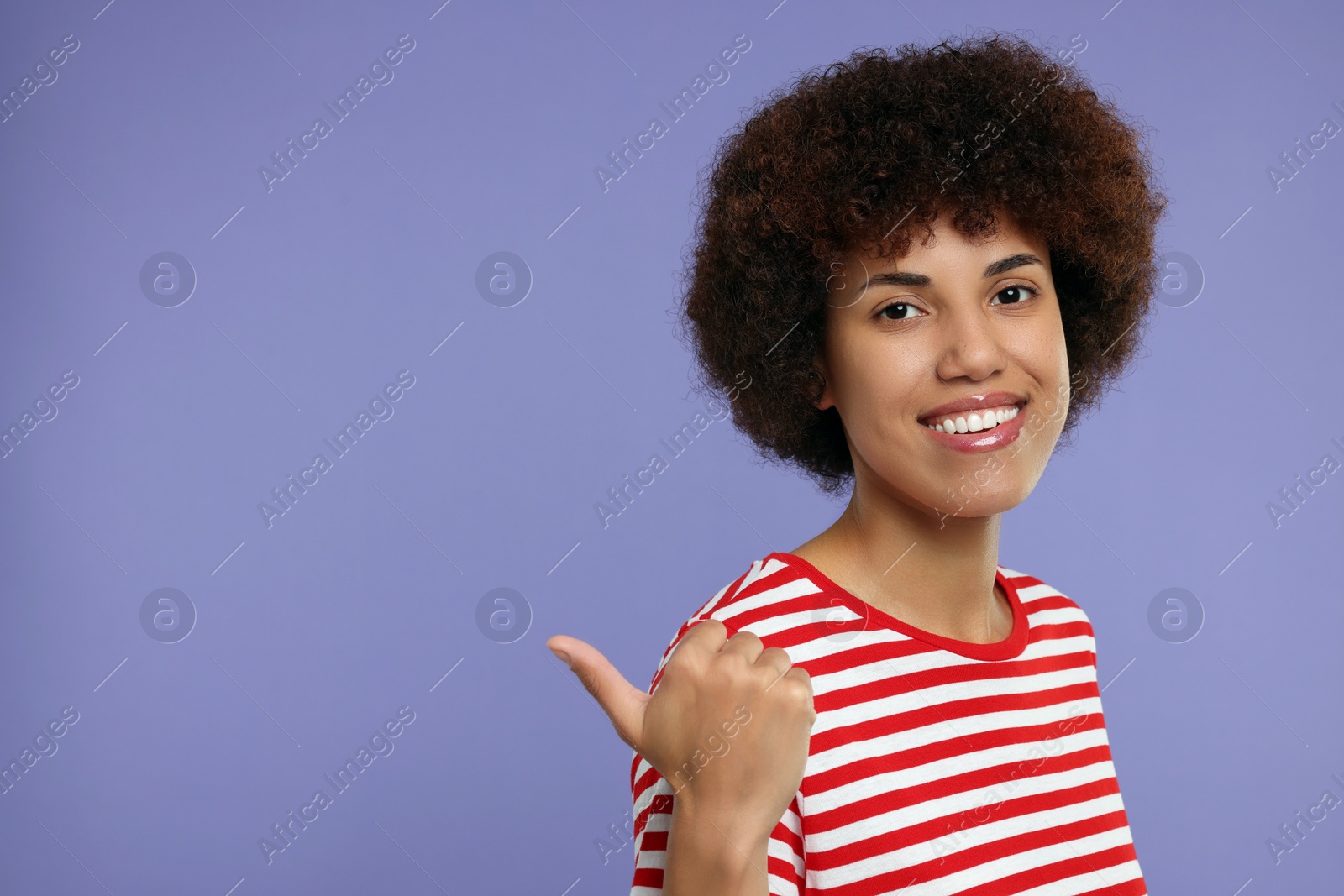 Photo of Happy young woman pointing at something on purple background. Space for text