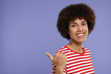 Photo of Happy young woman pointing at something on purple background. Space for text