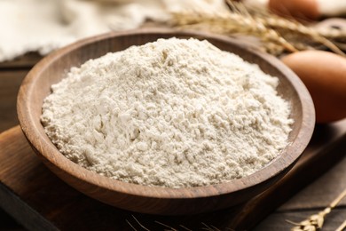 Bowl with wheat flour on wooden table, closeup