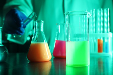 Photo of Scientist working with laboratory glassware of luminous liquids at table, selective focus