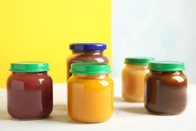 Photo of Jars with baby food on white wooden table against color background