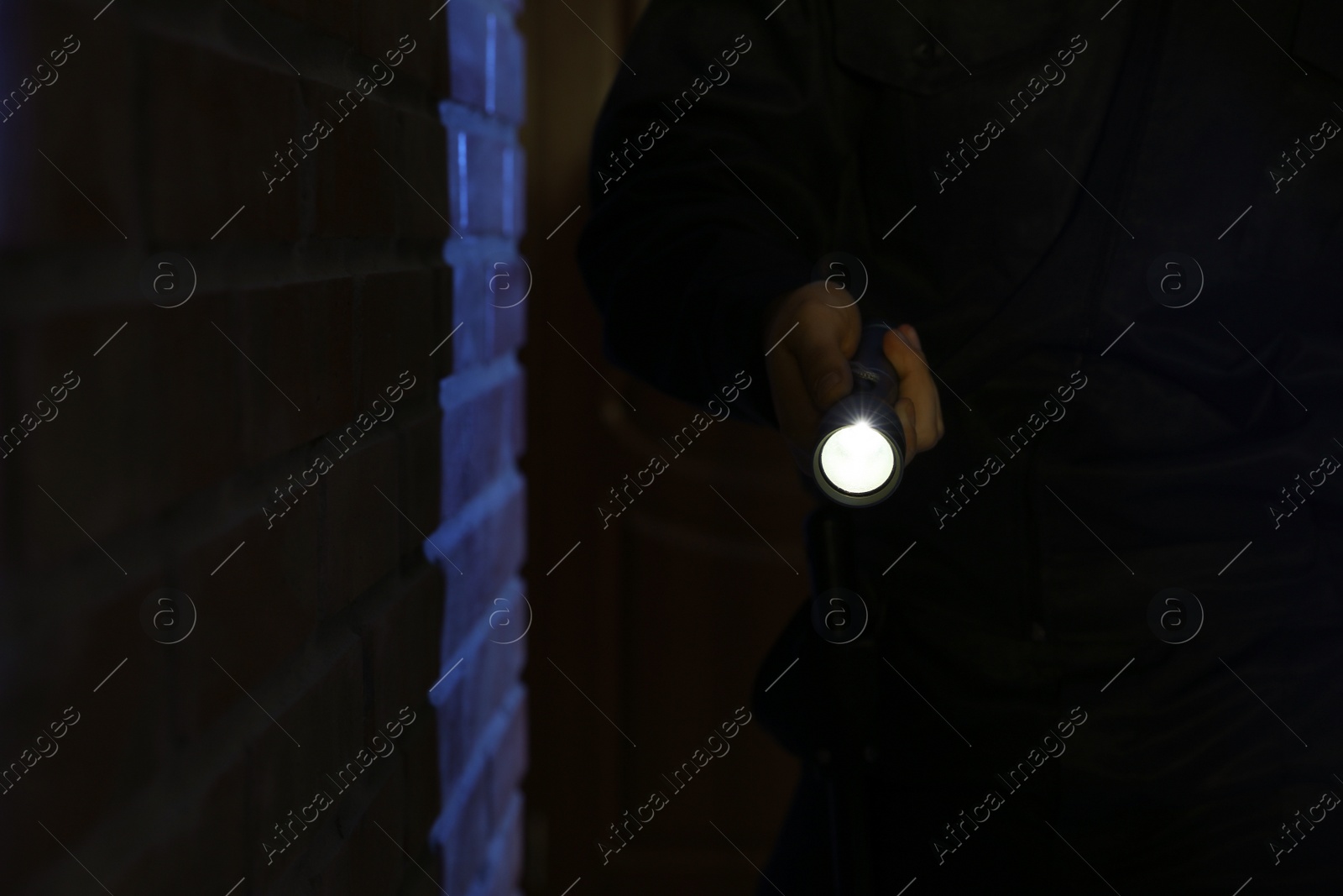Photo of Male security guard with flashlight near brick wall in darkness