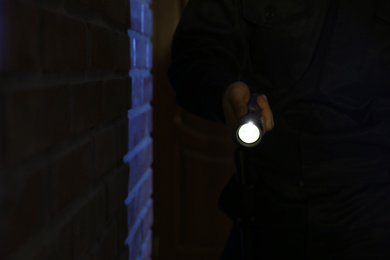 Photo of Male security guard with flashlight near brick wall in darkness