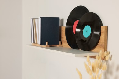 Photo of Wooden shelf with vinyl records and books on white wall