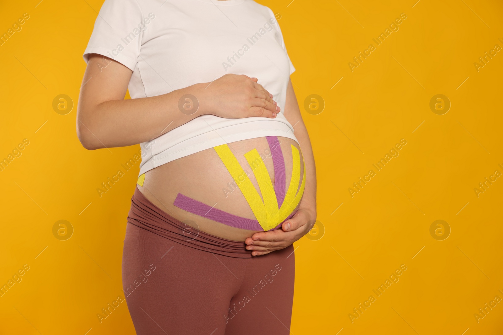 Photo of Pregnant woman with kinesio tapes on her belly against orange background, closeup. Space for text