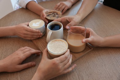 Photo of Friends drinking coffee at wooden table in cafe, closeup