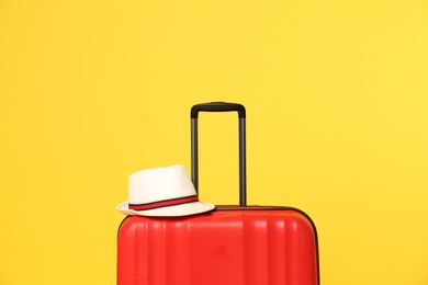 Photo of Bright suitcase with hat on color background