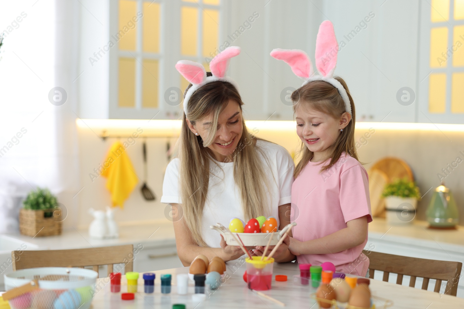 Photo of Easter celebration. Happy mother and her cute daughter with painted eggs at white marble table in kitchen