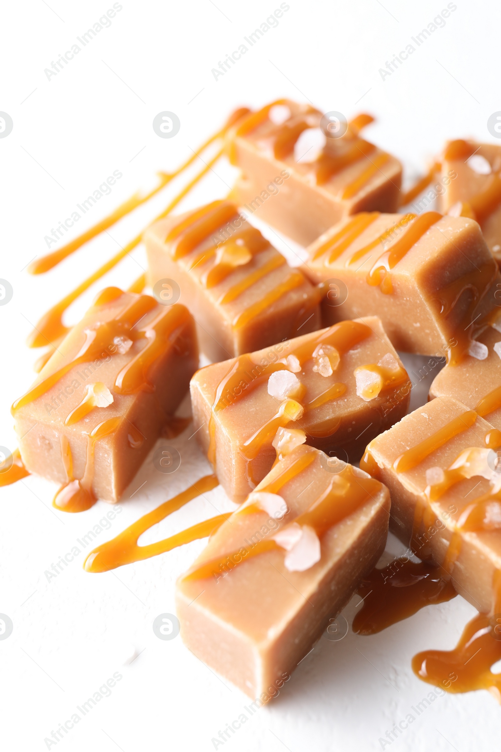 Photo of Tasty candies, caramel sauce and salt on white table, closeup