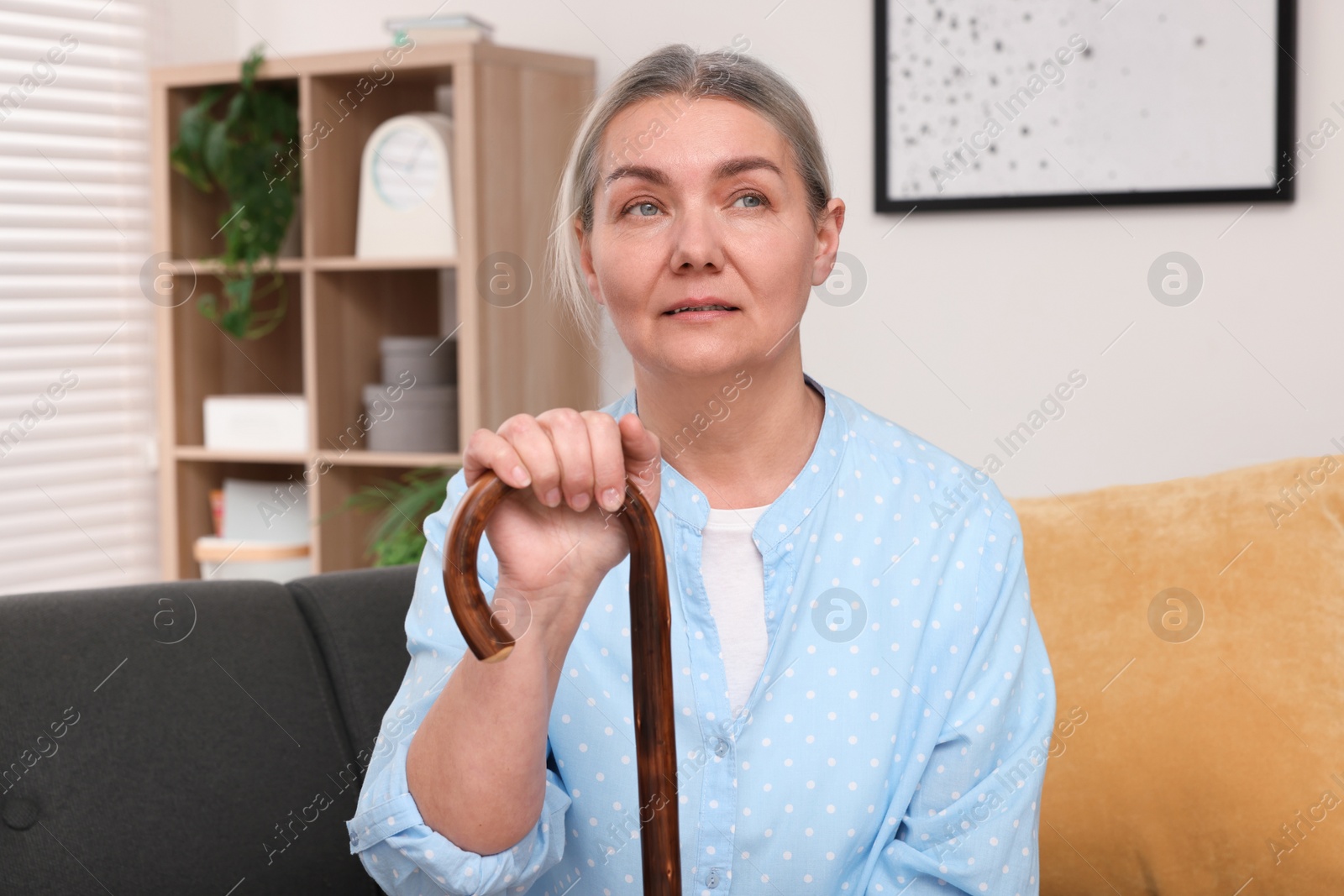 Photo of Senior woman with walking cane sitting on sofa at home