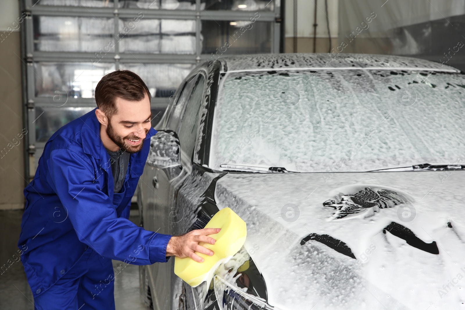 Photo of Worker cleaning automobile with sponge at professional car wash
