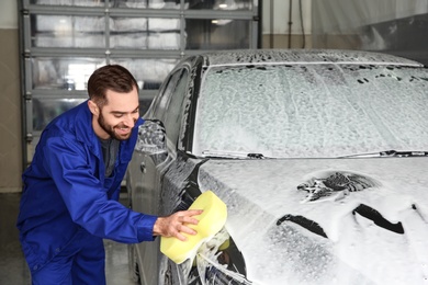 Worker cleaning automobile with sponge at professional car wash