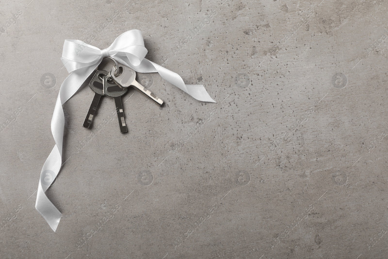 Photo of Keys with white bow on grey table, top view and space for text. Housewarming party