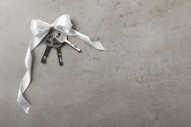 Photo of Keys with white bow on grey table, top view and space for text. Housewarming party