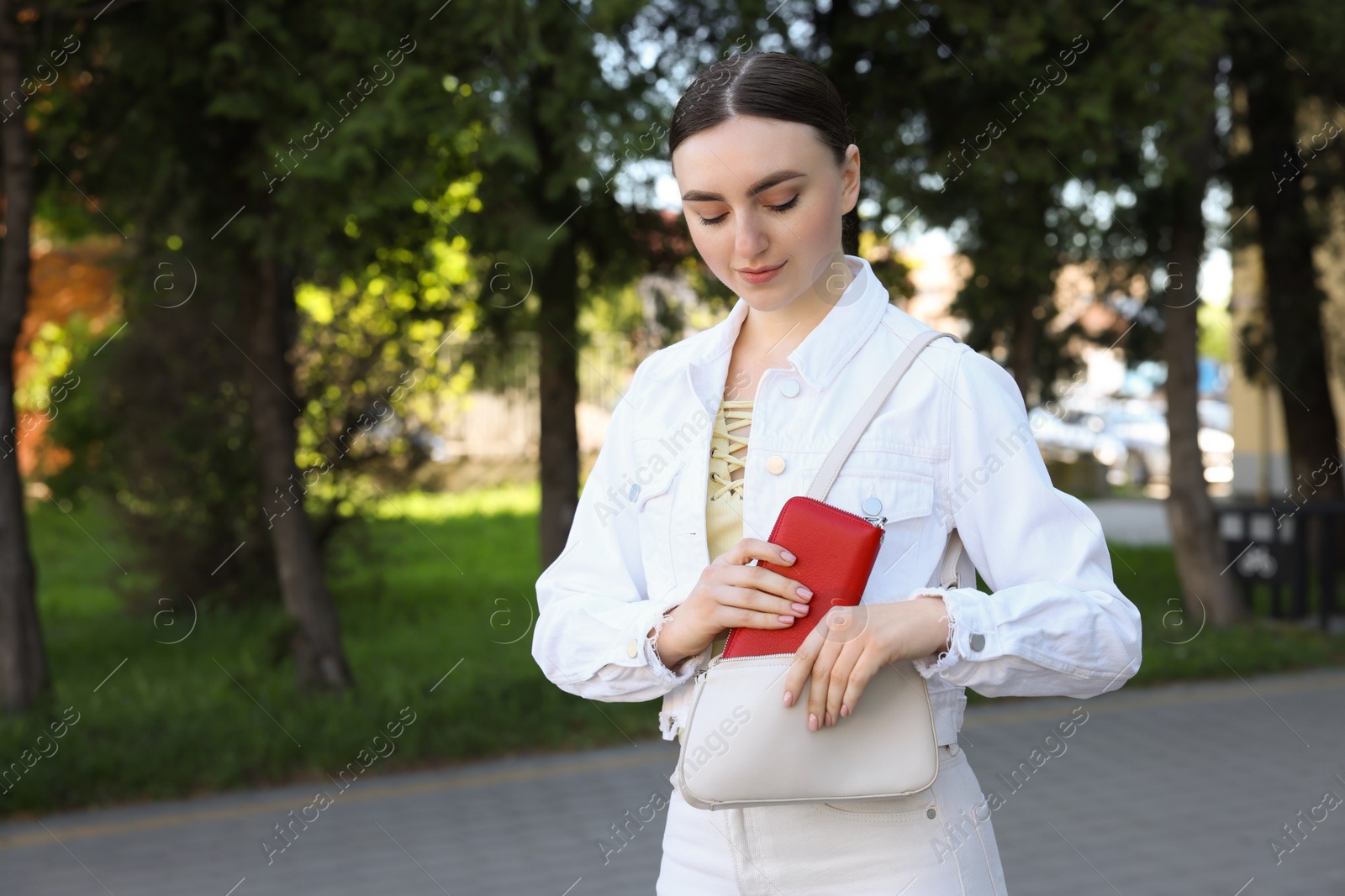 Photo of Young woman putting purse into bag outdoors, space for text