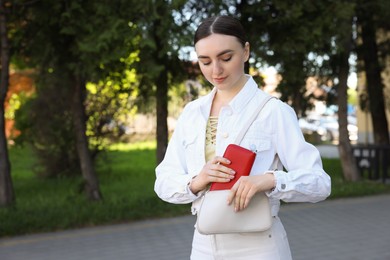 Young woman putting purse into bag outdoors, space for text