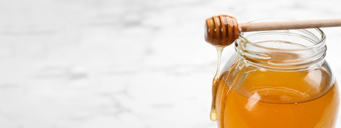 Image of Tasty honey on white marble table, closeup view with space for text. Banner design