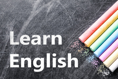 Pieces of color chalk on blackboard, flat lay. Learn English