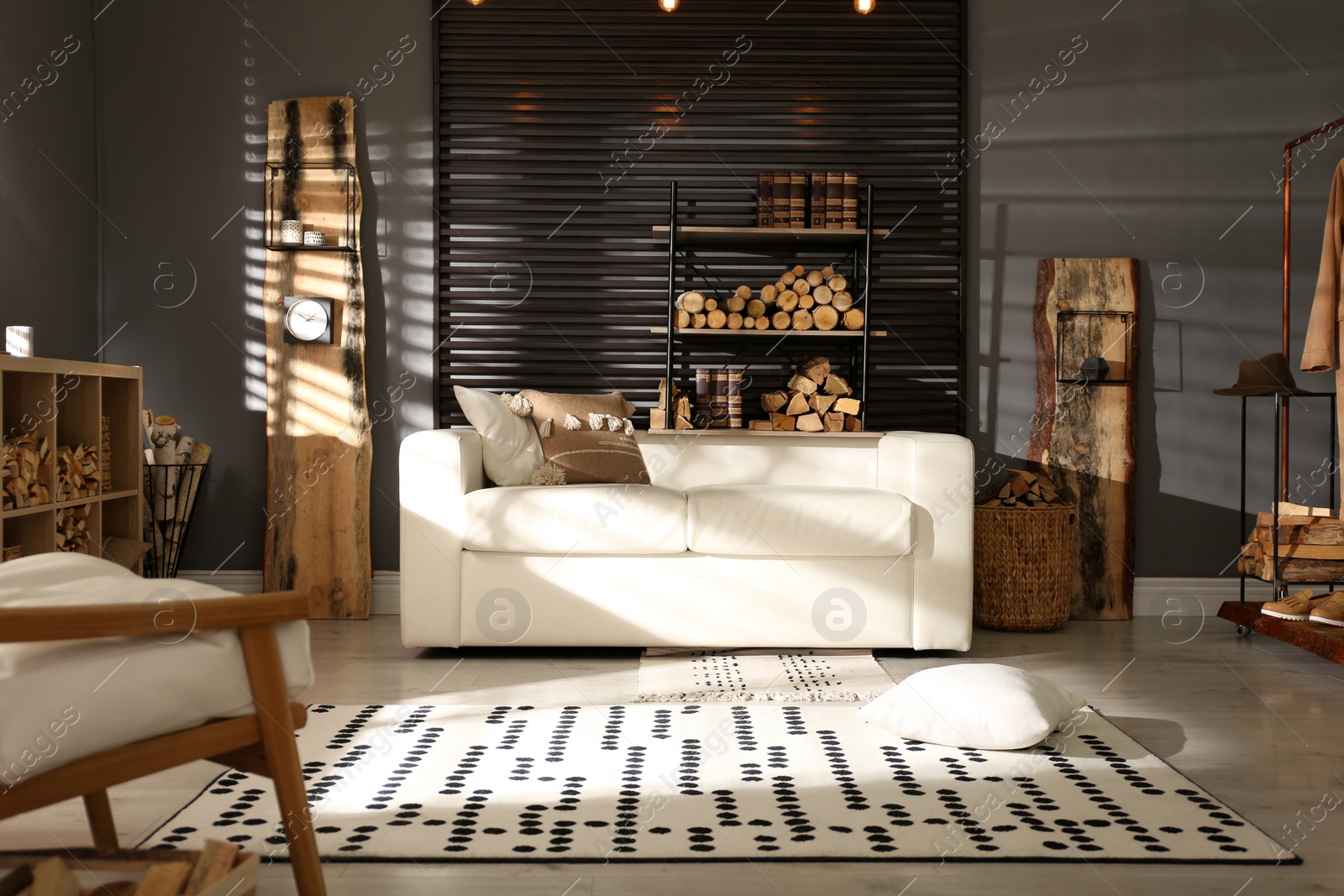 Photo of Shelving unit with stacked firewood and comfortable sofa in stylish room interior