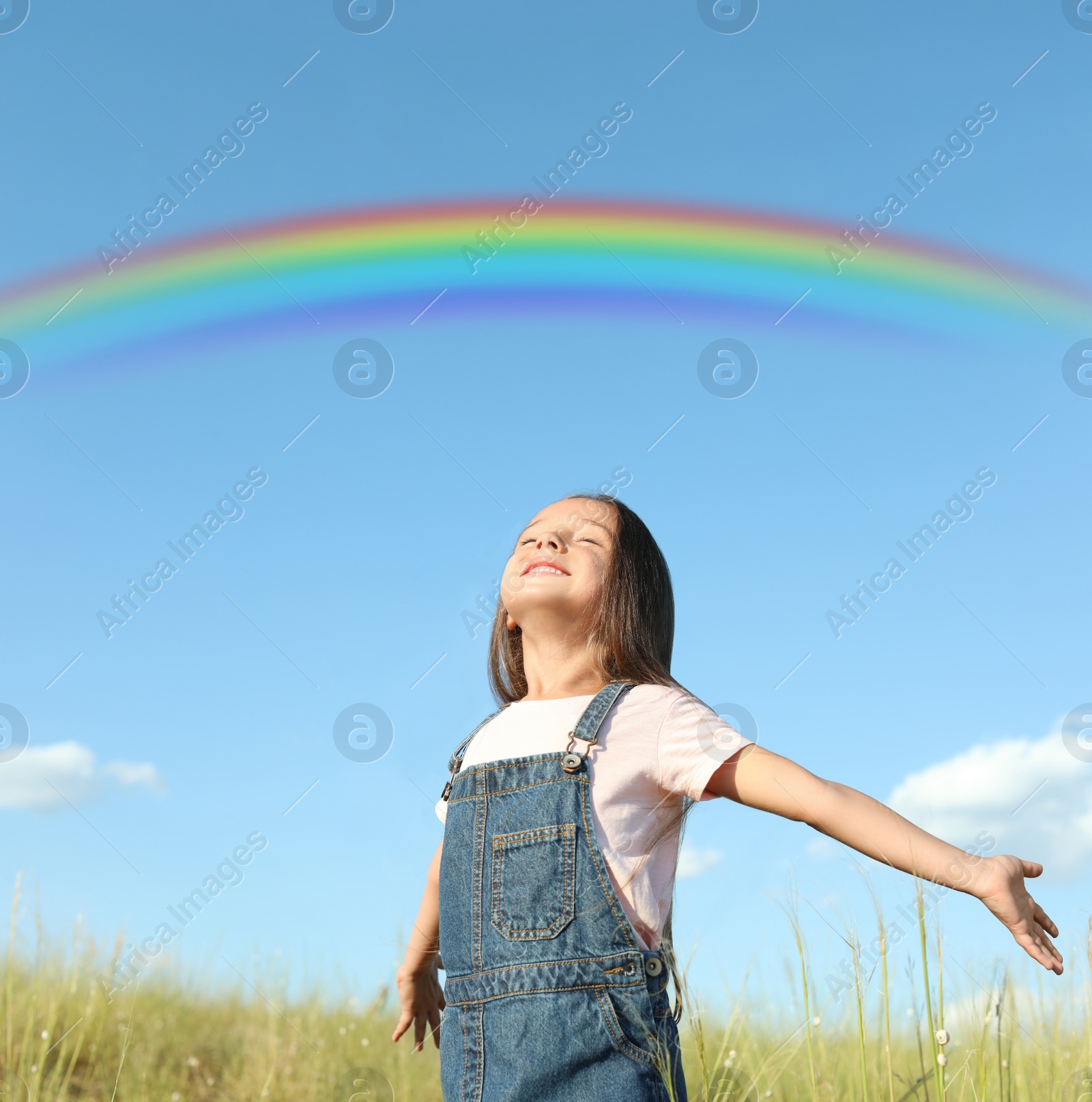 Image of Beautiful rainbow in blue sky over cute little girl in field on sunny day