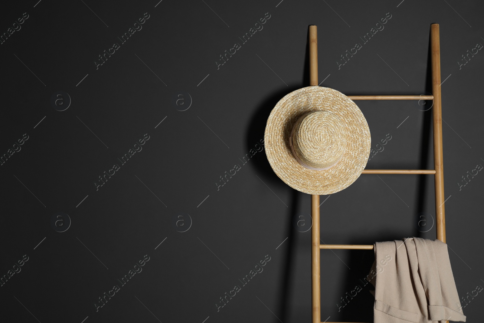 Photo of Straw hat and jacket on ladder near dark wall. Space for text