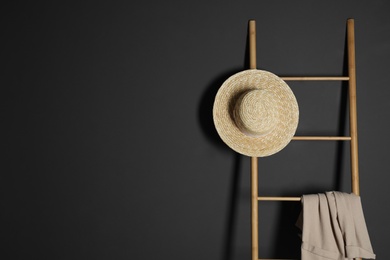 Straw hat and jacket on ladder near dark wall. Space for text