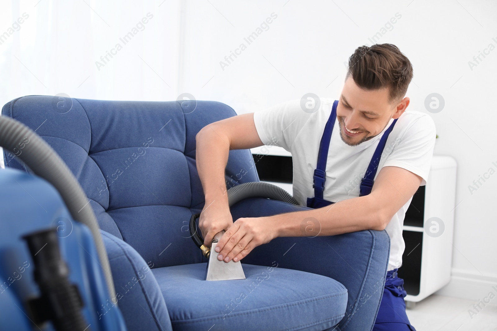 Photo of Dry cleaning worker removing dirt from armchair indoors