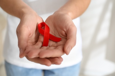 Photo of Woman holding red awareness ribbon on light background, closeup with space for text. World AIDS disease day