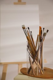 Photo of Holder with brushes and spatula near wooden easel in art studio