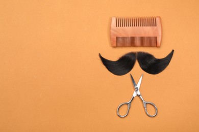 Photo of Artificial moustache, comb and scissors on orange background, top view. Space for text