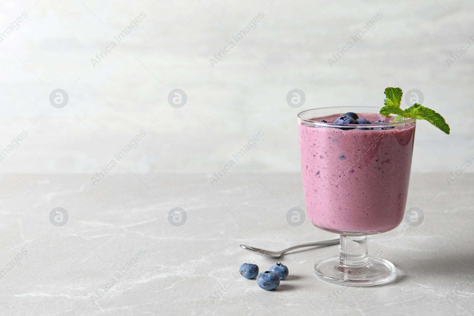 Photo of Glass with blueberry smoothie on grey table. Space for text