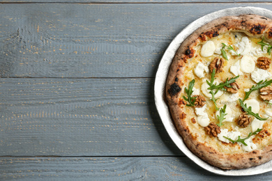 Photo of Delicious cheese pizza with walnuts and arugula on grey wooden table, top view. Space for text