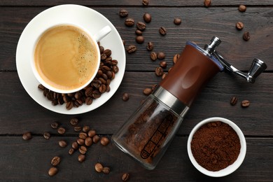 Photo of Modern manual coffee grinder with powder, beans and cup of aromatic drink on wooden table, flat lay