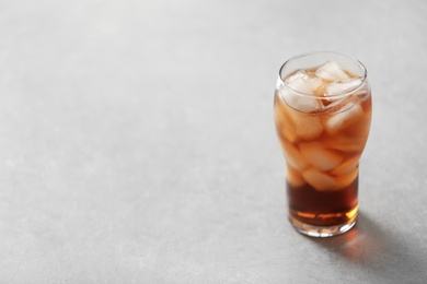 Glass of cola with ice on light background, space for text