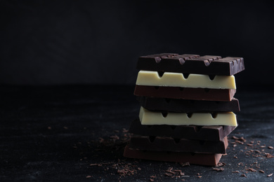 Photo of Different tasty chocolate bars on black table. Space for text