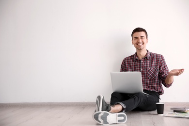 Photo of Young blogger with laptop sitting on floor against light wall